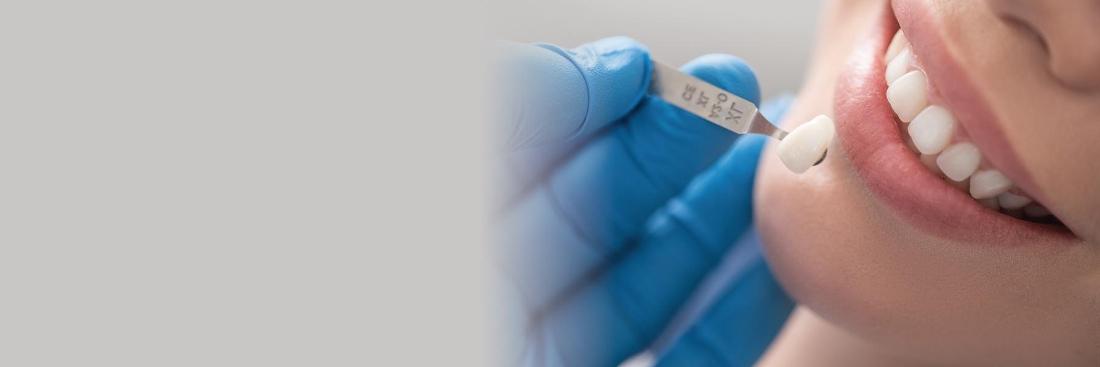 dentist with blue gloves holding a tooth sample up to a woman's mouth