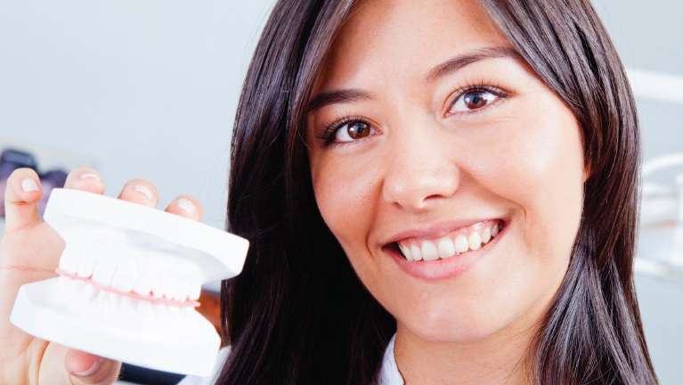A smiling woman holding a dental mold